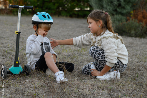 Wallpaper Mural A young boy in a helmet riding a scooter falls and scrapes his knee. A girl approaches him, showing empathy and sprays medicine on his knee to help soothe the injury.
 Torontodigital.ca