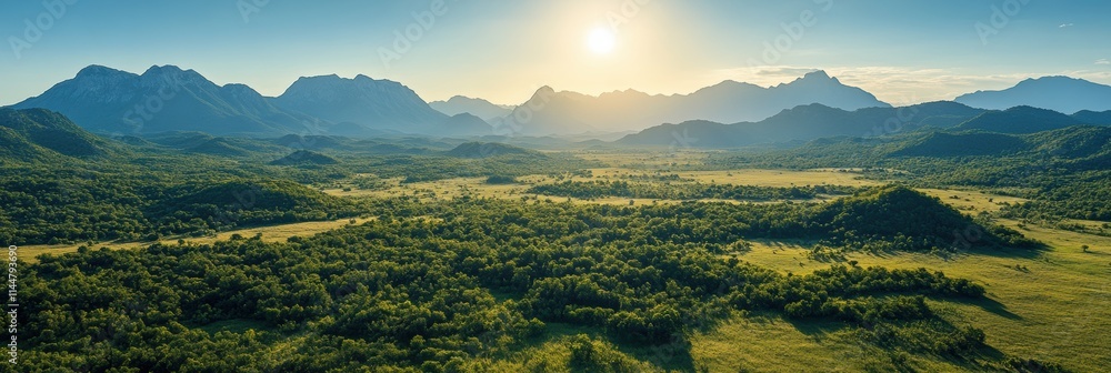 Fototapeta premium A breathtaking panoramic view showcasing a lush, expansive valley with rolling hills and towering mountains under a golden sunrise, illustrating the stunning beauty of untouched natural landscapes