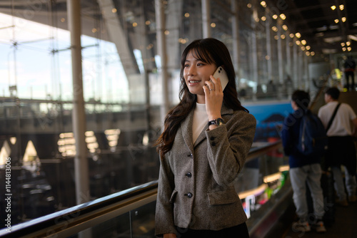 Young asian businesswoman is using her smartphone while riding a moving walkway in a modern airport terminal, showcasing connectivity and efficiency in business travel photo