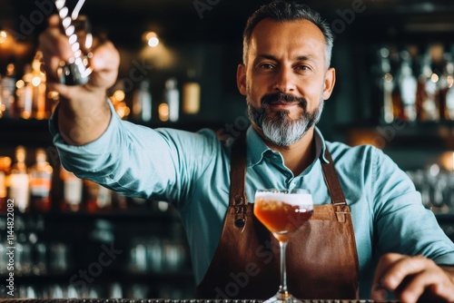 The bartender skillfully pours a cocktail into a sleek glass, wearing a teal shirt with a brown apron, set against a backdrop of a stylishly lit bar interior. photo