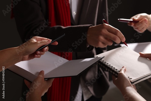 Man signing autograph in notebook on dark background, closeup photo