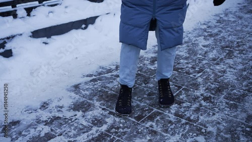 Winter season brings icy sidewalks, requiring careful navigation to avoid slips and falls, as demonstrated by a woman cautiously walking on a frozen path