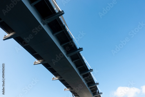 Slightly curved modern steel hanging bridge overpass from below against blue sky in summer for transportation and infrastructure concept