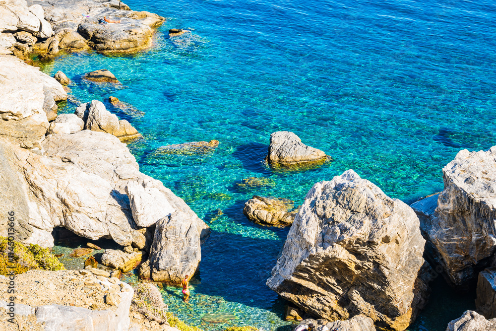 Unidentified woman standing in sea water among rocks near Agia Anna beach, Amorgos island, Cyclades, Greece