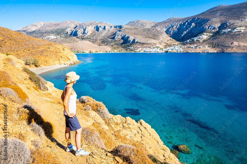 Woman tourist standing on high cliff and looking at Hochlaka beach in Aigiali bay (Ormos Egialis), Amorgos island, Cyclades, Greece
