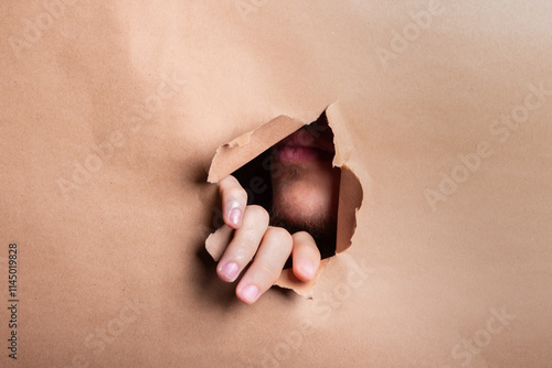 A mans hand poking through a hole in a sheet of brown paper.