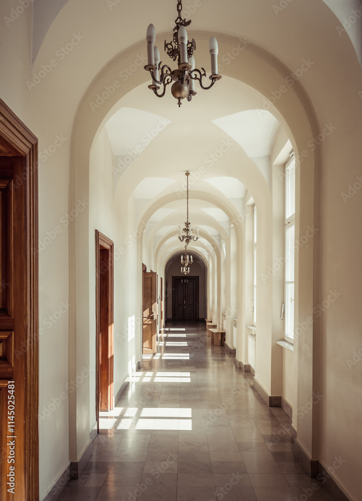 Beige arched corridor with tiled floor in 19th century building. Sunlight shines from windows on the right side.
Beige arched corridor with tiled floor in 19th century building. Sunlight shines from windows on the right side.