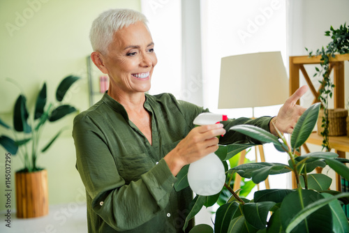 Photo of positive good mood woman dressed green shirt smiling watering plant indoors house apartment room photo