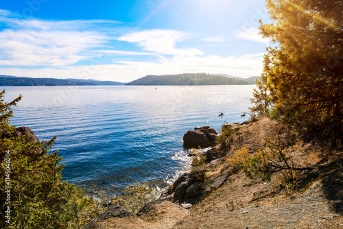 Fototapeta Naklejka Na Ścianę i Meble -  Two kayakers near the rocky shoreline of Tubbs Hill park and hiking trail on the lake in the downtown district of Coeur d'Alene, Idaho.