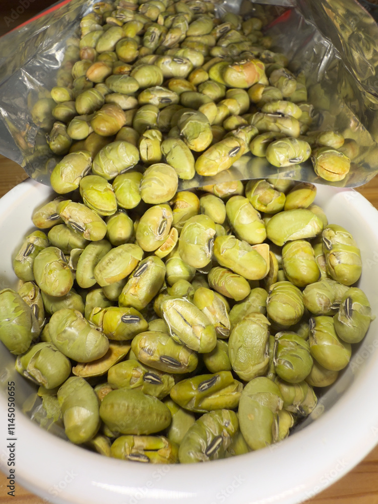 Macro closeup of crunchy, dry roasted Edamame beans snack pouring from a retail packet into a bowl, ready to eat. Macro closeup of crunchy, dry roasted Edamame beans snack pouring from a retail packet into a bowl, ready to eat.