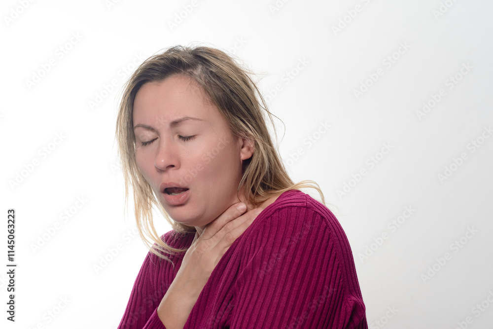 A woman with her eyes closed, wearing a dark pink ribbed sweater, coughs while holding her throat against a light background.