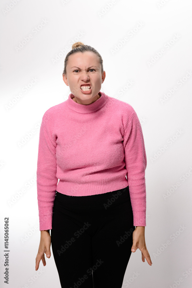 A woman in pink top and black pants stands against a white background, her face contorted in an expression of intense anger and frustration. A woman in pink top and black pants stands against a white background, her face contorted in an expression of intense anger and frustration.