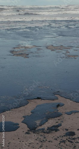 Sea and the beach are polluted with fuel oil. Coastline oil spill impact, pollution, waste disposal. Vertical screen