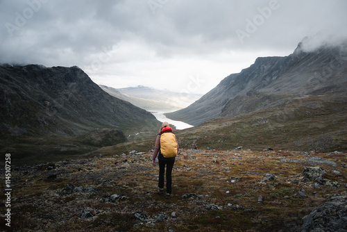 Hiker explores Norwegian valley with cloudy sky and dramatic landscapes. photo