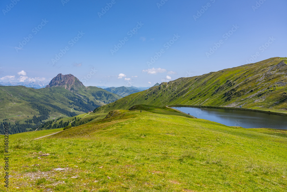 Fototapeta premium Visitors enjoy the breathtaking views of the Wildkogel water reservoir. Surrounded by the stunning peaks of the Austrian Alps, the area offers tranquility and natural beauty.