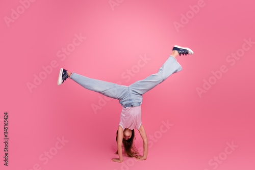 Photos Young girl in casual outfit performing a fun handstand against a vibrant pink st