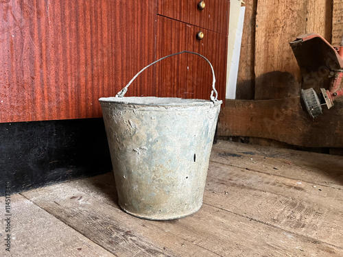 Old metal bucket resting on weathered wooden floor next to cabinets in a rustic interior setting