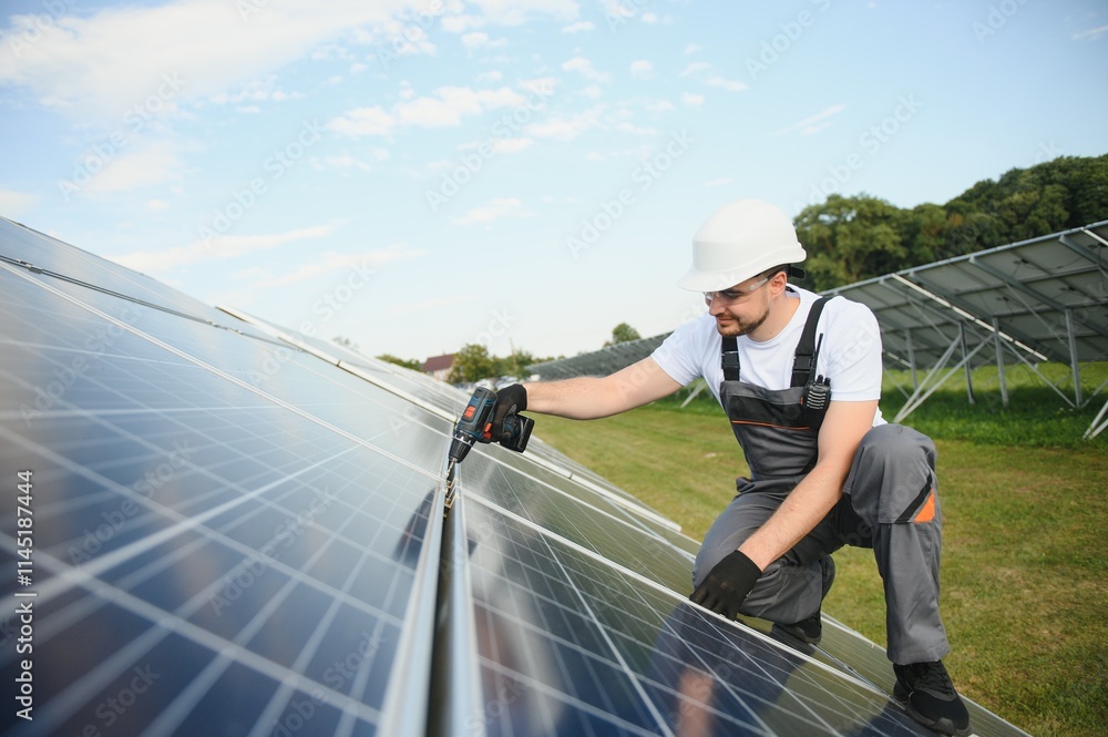Side view of male worker installing solar modules and support structures of photovoltaic solar array. Electrician wearing safety helmet Side view of male worker installing solar modules and support structures of photovoltaic solar array. Electrician wearing safety helmet