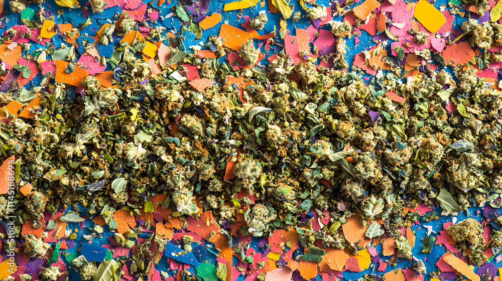 A textured blend of crushed marijuana and sticky buds arranged on a bright multicolored ground.