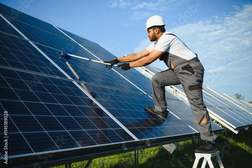 Professional indian worker cleans solar panels with brush, green electric power technology photo