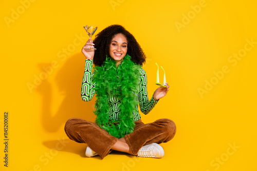 Young woman with black curly hair in green top and sunglasses joyfully celebrates against a vibrant yellow background. photo