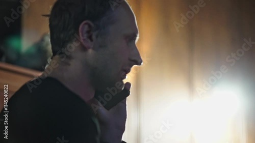 A man is captured in a close-up, engaged in a phone conversation. The warm, indoor lighting and his focused expression suggest an important or perhaps serious discussion