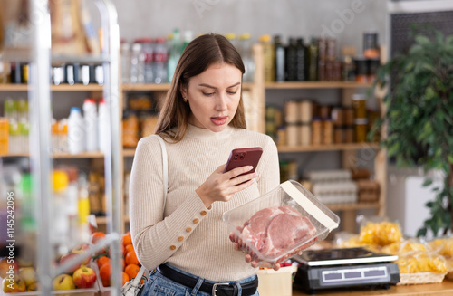 Girl scan QR-code on raw pork package in store. Market visitor choose consider dried meat delicious. Buyer pick up set of snack for party photo