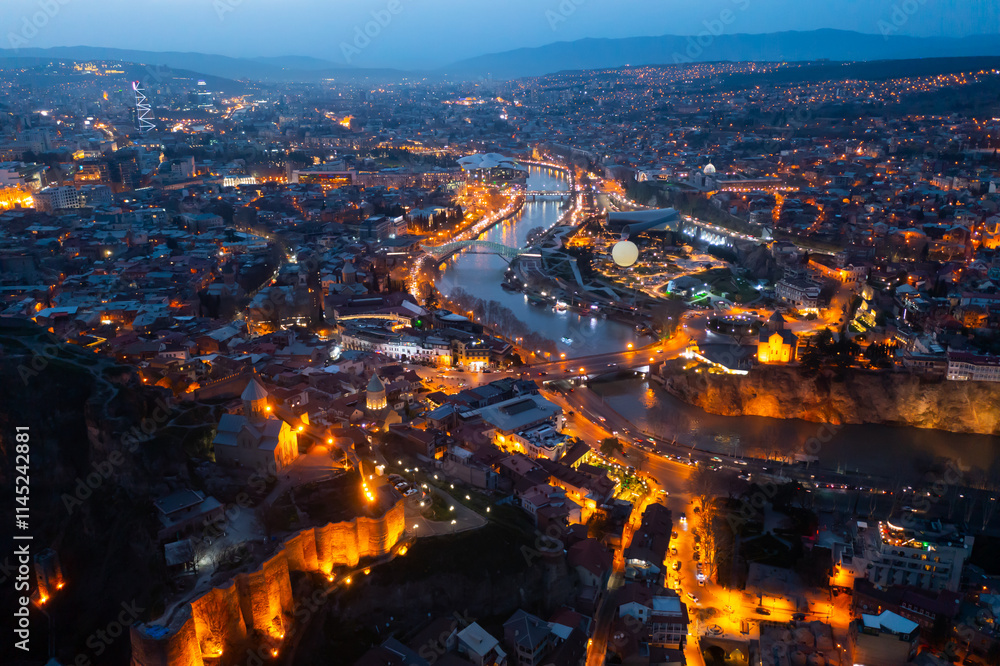 Obraz premium Aerial panoramic view of illuminated historic center of Tbilisi city on banks of Mtkvari River on spring twilight, Georgia