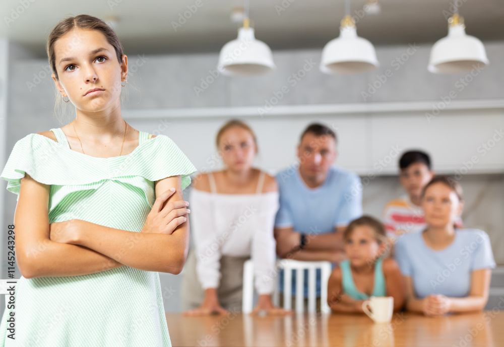Miffed pre-teen girl with arms crossed over chest standinf in front of her big family Miffed pre-teen girl with arms crossed over chest standinf in front of her big family