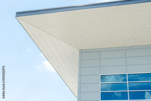 The exterior corner of a modern building with a flat roof, grey eave, white soffit, and contemporary metal aluminum composite panels. There are small blue glass windows with the blue sky reflecting. photo