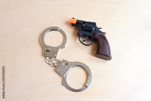 A pair of handcuffs with a fake revolver on a wood background. Toys or cinema accessories representing metal handcuffs and a gun. Criminal capture and prison. Criminal offense, law and jail. photo