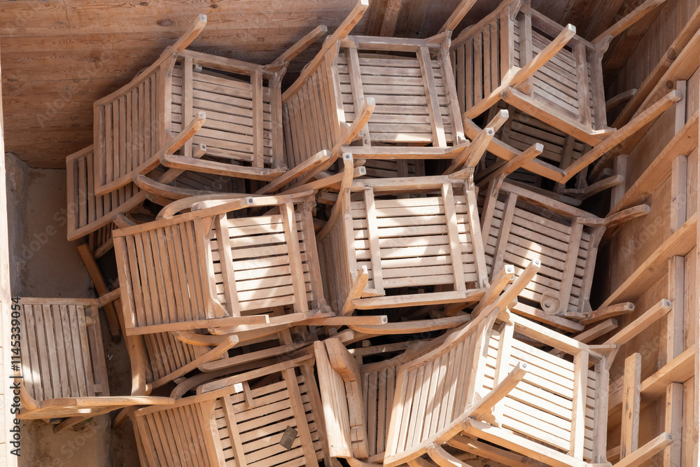 Rustic wooden chairs stacked in sunlit storage space for outdoor seating arrangement inspiration Rustic wooden chairs stacked in sunlit storage space for outdoor seating arrangement inspiration