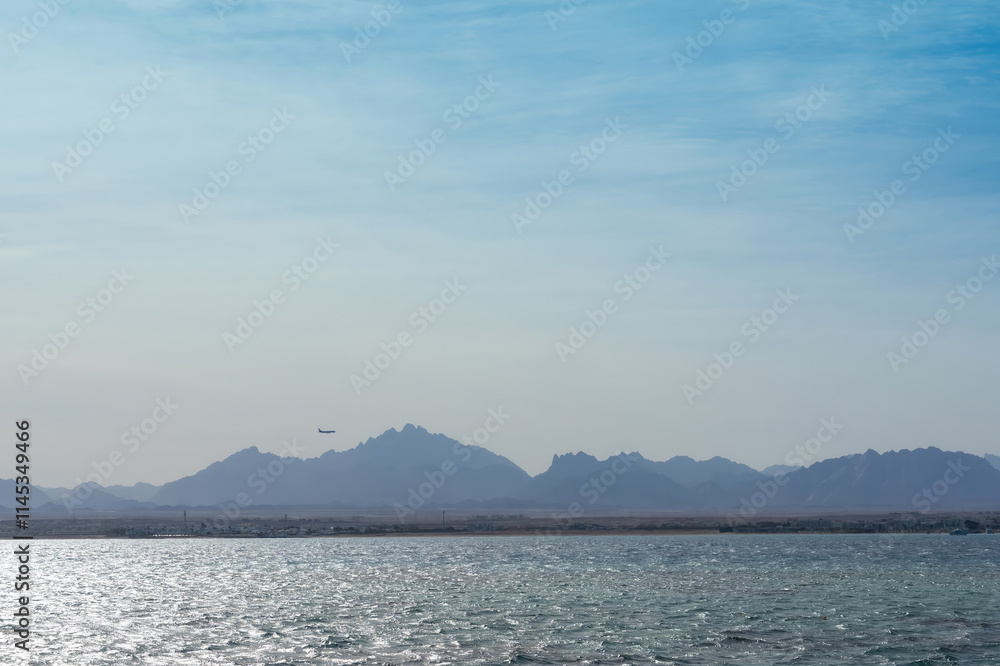 Tranquil seascape with distant mountains and airplane under clear sky Tranquil seascape with distant mountains and airplane under clear sky