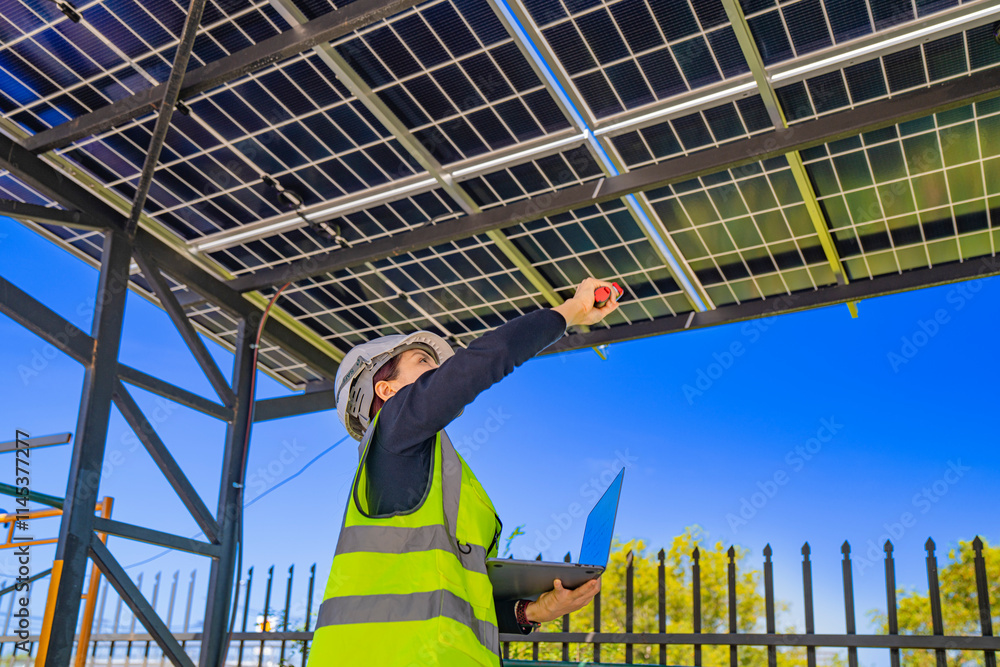Fototapeta premium Engineer in safety vest and helmet pointing towards a solar powered carport, illustrating eco-friendly innovation in parking infrastructure. Solar panels provide shade and sustainable energy.