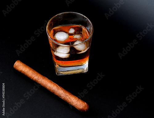 A glass of old whiskey with ice cubes and a large Cuban cigar on a black background. photo