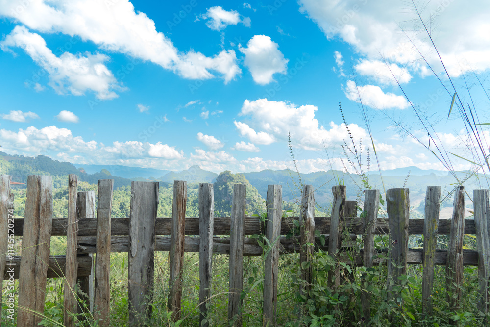 Fototapeta premium Wooden fence overlooks a scenic view of rolling hills. Under view of bright blue sky with fluffy white clouds. Traveling in Thailand of village Ban Jabo Mae Hong Son.