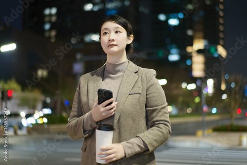 Professional Woman in Urban Scene at Night with Coffee and Smartphone photo