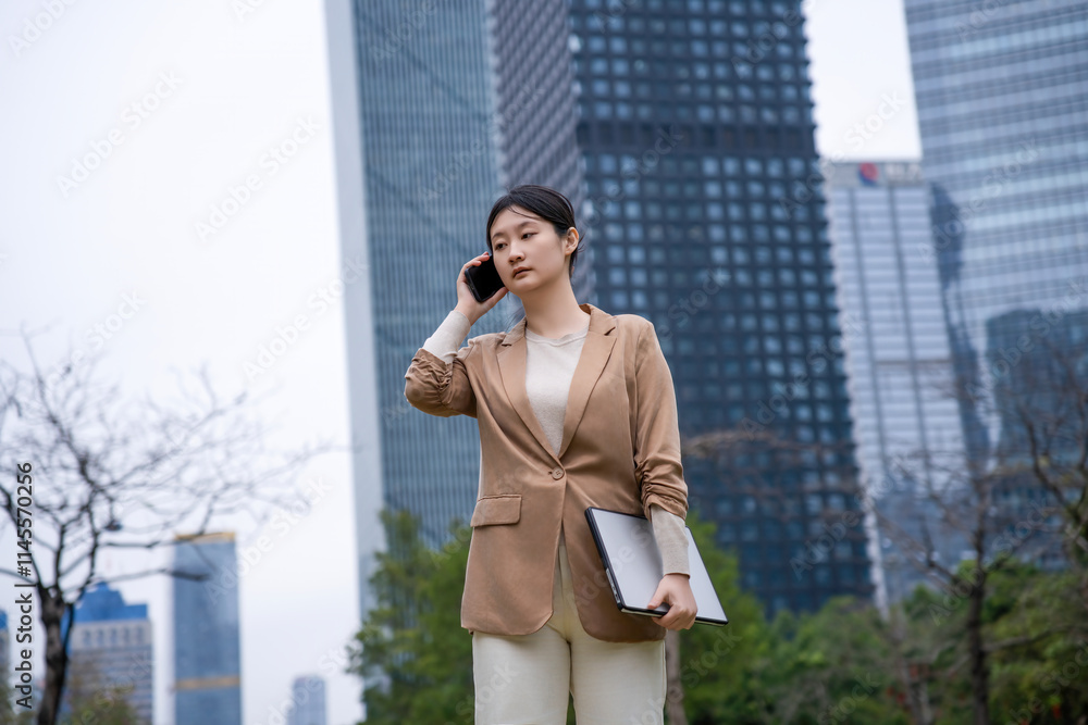 Confident Businesswoman in Urban Setting Holding a Laptop and Phone Confident Businesswoman in Urban Setting Holding a Laptop and Phone