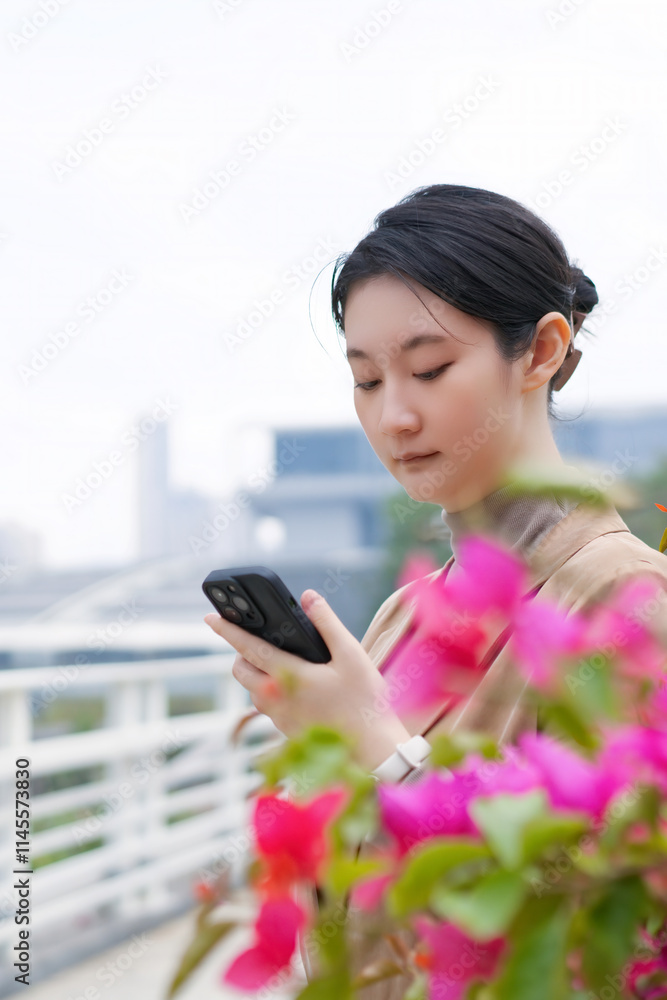 A Young Woman in Traditional Garb Engaged with Her Smartphone Amid Vibrant Blossoms A Young Woman in Traditional Garb Engaged with Her Smartphone Amid Vibrant Blossoms
