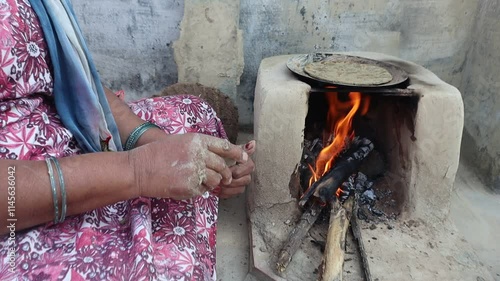 Indian woman cooking bajre ki roti on a traditional clay chulha, showcasing rural lifestyle and traditional cooking methods. photo