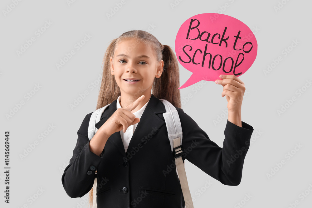 Cute little girl in school uniform pointing at speech bubble with text BACK TO SCHOOL on grey background Cute little girl in school uniform pointing at speech bubble with text BACK TO SCHOOL on grey background