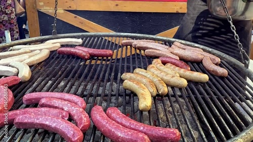 A man cooks large sausages with different meats on an open grill outside. Pork, chicken, beef sausages.