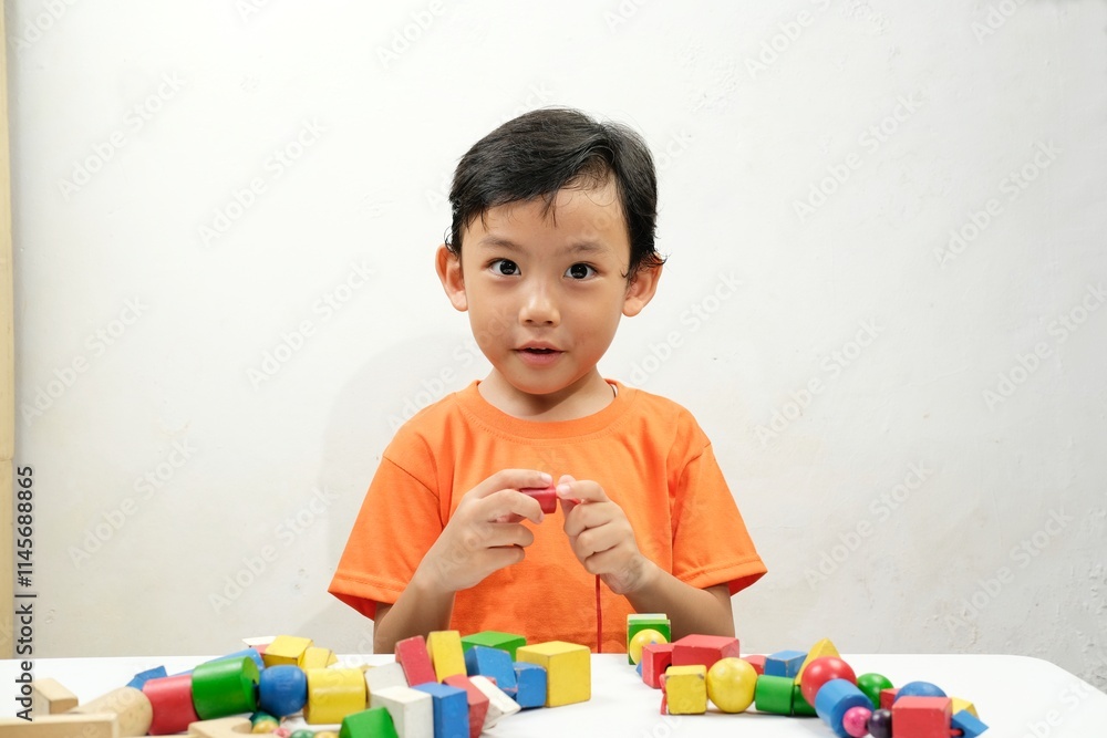 A young boy intently threads colorful wooden beads, developing fine motor skills and creativity. Perfect for educational content on child development, learning, and fun activities. A young boy intently threads colorful wooden beads, developing fine motor skills and creativity. Perfect for educational content on child development, learning, and fun activities.