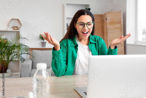 Beautiful young woman video chatting with laptop on table at home