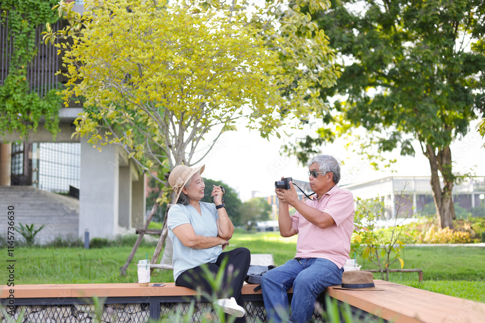 Senior couple in park, Asian senior man taking pictures of his woman sitting outdoors Senior couple in park, Asian senior man taking pictures of his woman sitting outdoors