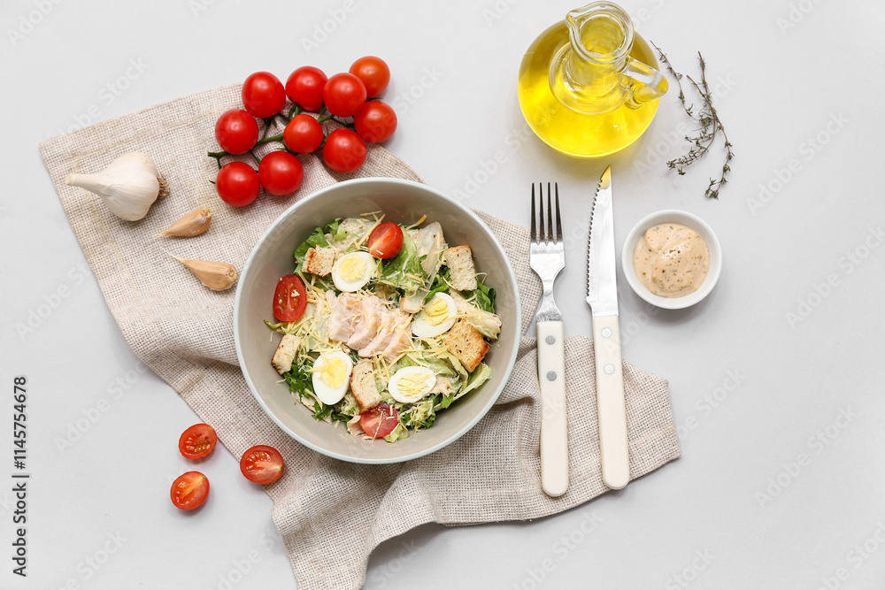 Bowl of tasty chicken Caesar salad with tomatoes, garlic and bowl of sauce on grey background Bowl of tasty chicken Caesar salad with tomatoes, garlic and bowl of sauce on grey background
