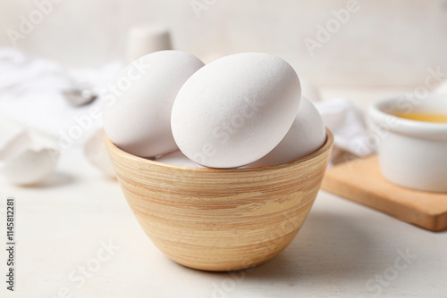 Bowl with raw chicken eggs on white wooden table photo