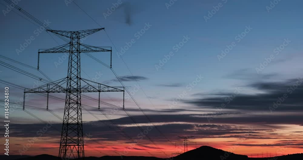 Time-lapse of a beautiful sky during sunset contrasting with a hilly landscape with massive poles with overhead high voltage power lines