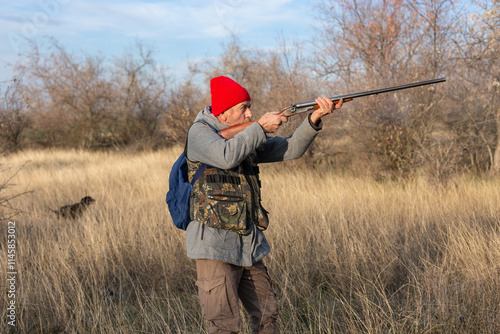 Mature hunter man holding a shotgun and walking through a field photo