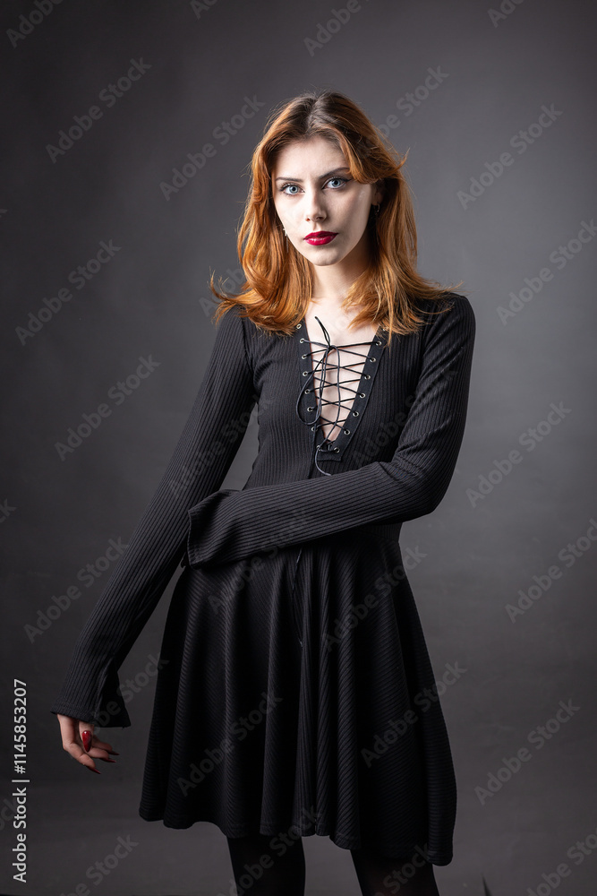 Red-haired gothic girl in a black dress on a gloomy background in the studio. Red-haired gothic girl in a black dress on a gloomy background in the studio.